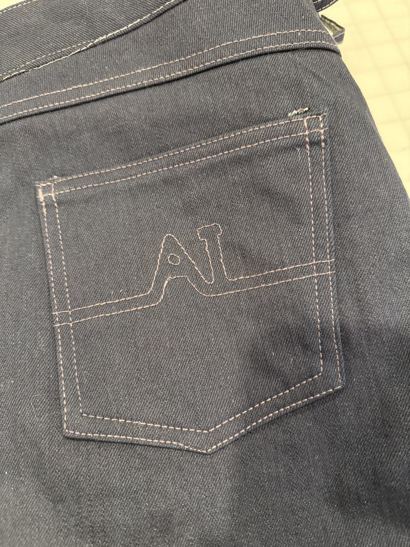 Close view of one back pocket with a monogram stitched in gold thread.