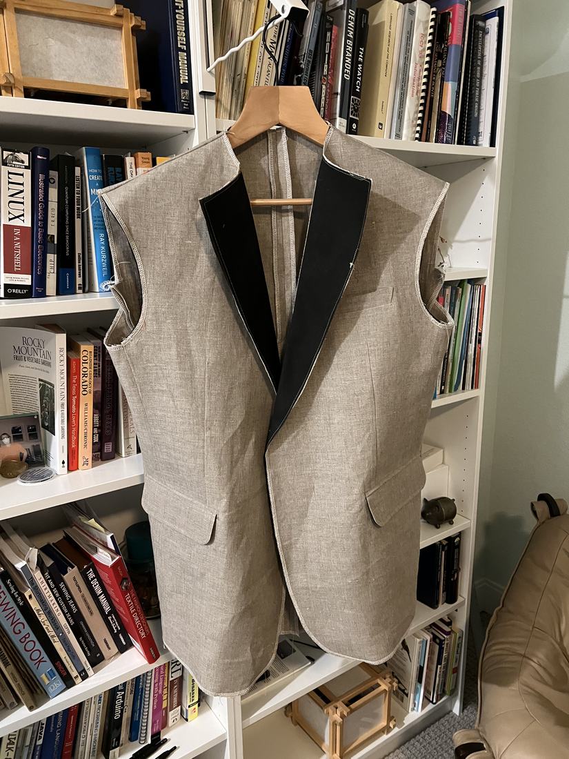 The linen jacket body on a hanger before the sleeves are attached, with dark interfacing pinned along both lapels.