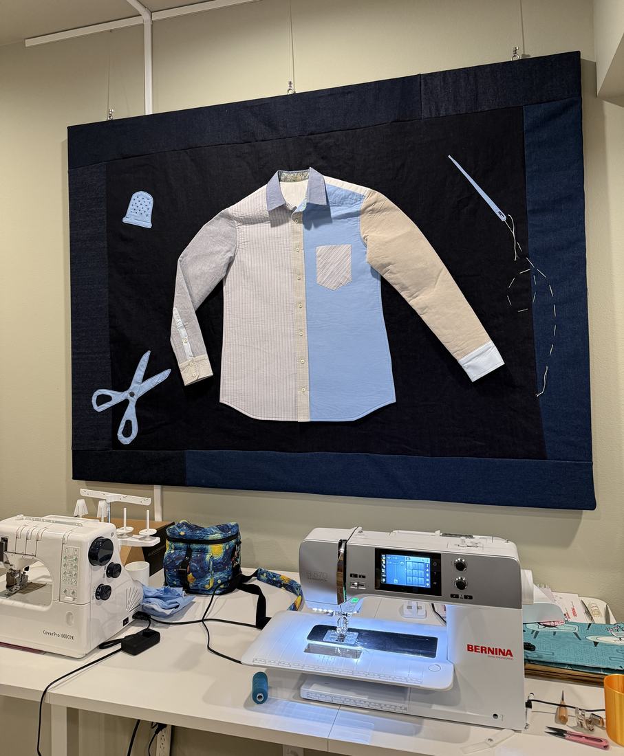 A large denim-bordered wall hanging of a shirt pieced from different shirtings, hung above two sewing machines.