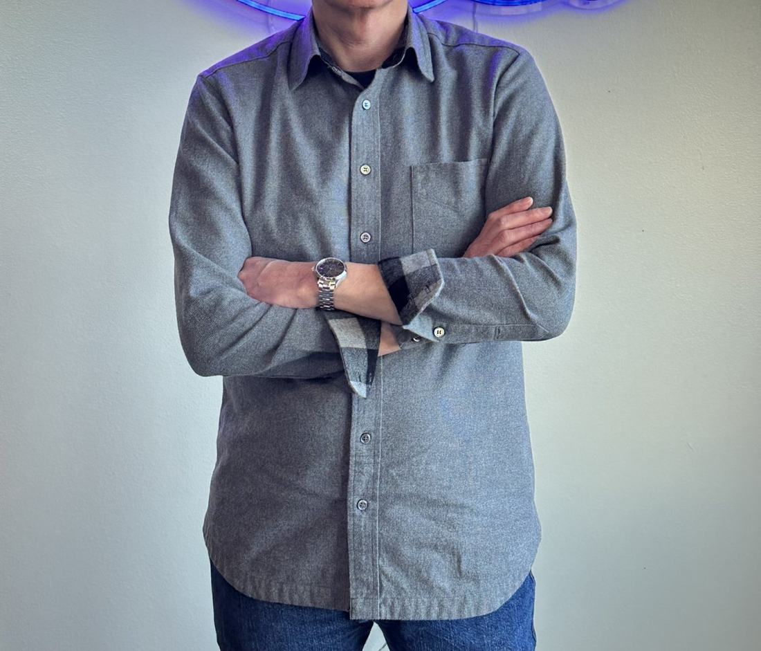 The grey flannel shirt worn, arms crossed, in front of a neon Sew Inspired sign.